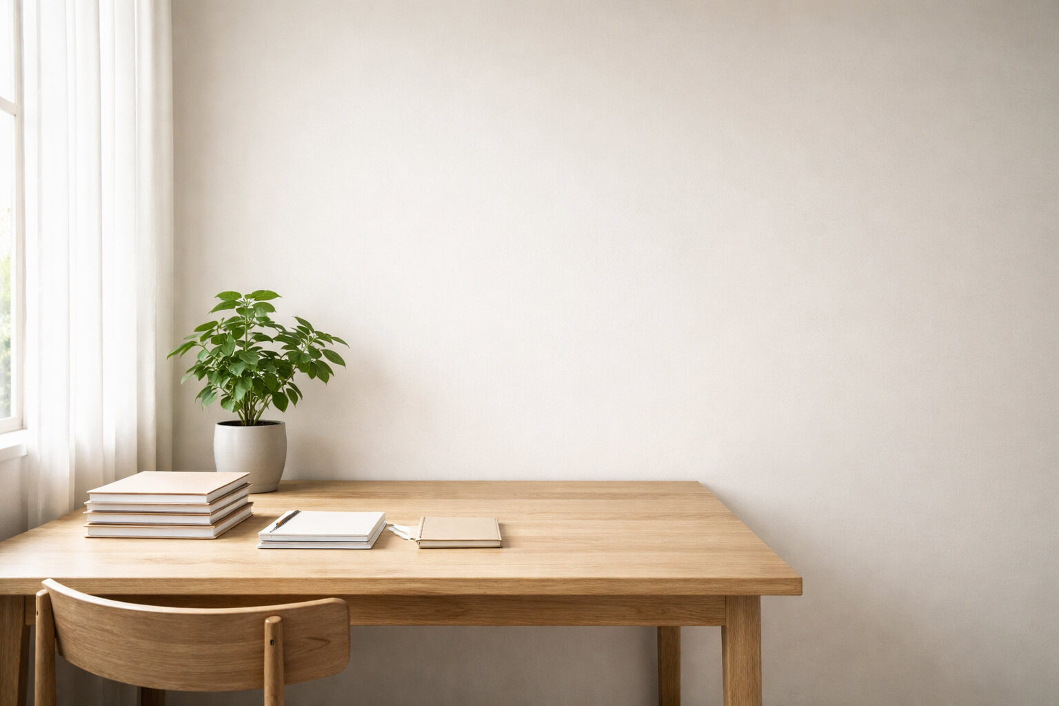 Mesa de madera clara junto a una ventana con luz natural difusa, cuadernos ordenados y una planta en maceta sobre fondo neutro.