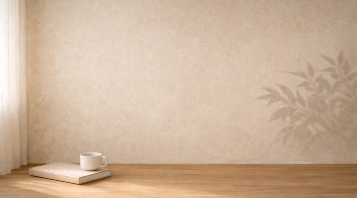 Interior minimalista con pared beige iluminada por luz natural, un libro cerrado y una taza blanca sobre suelo de madera en un ambiente tranquilo de reflexión.
