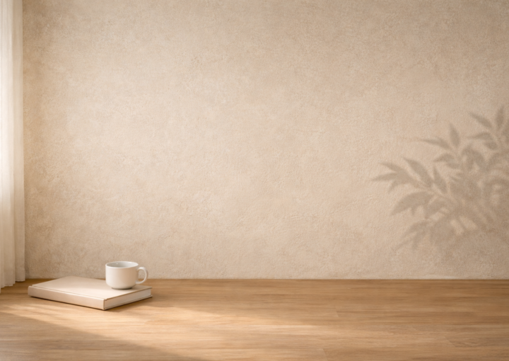 Interior minimalista con pared beige iluminada por luz natural, un libro cerrado y una taza blanca sobre suelo de madera en un ambiente tranquilo de reflexión.